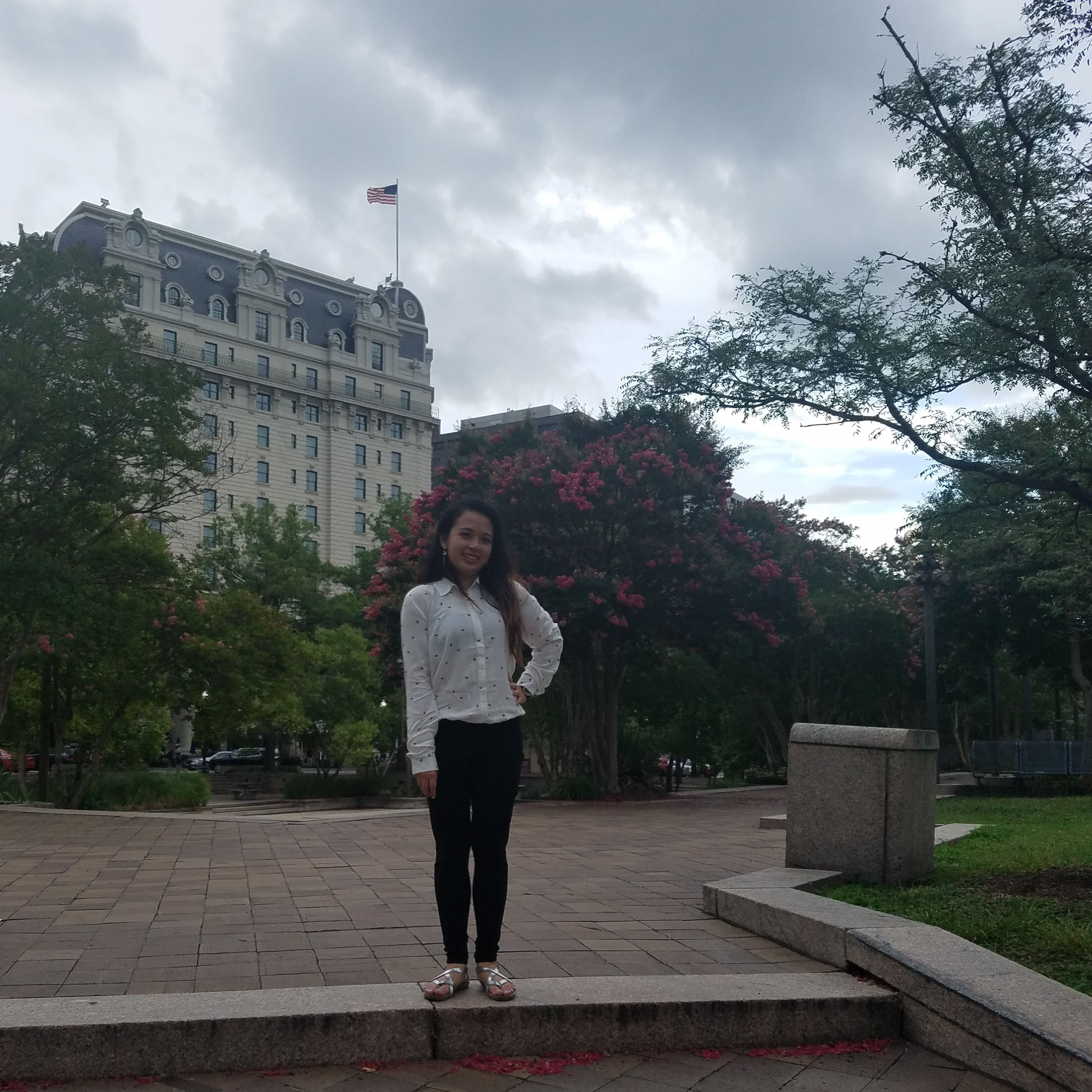 A photo of me with the picture perfect background of the sun breaking across the clouds and some flowers.