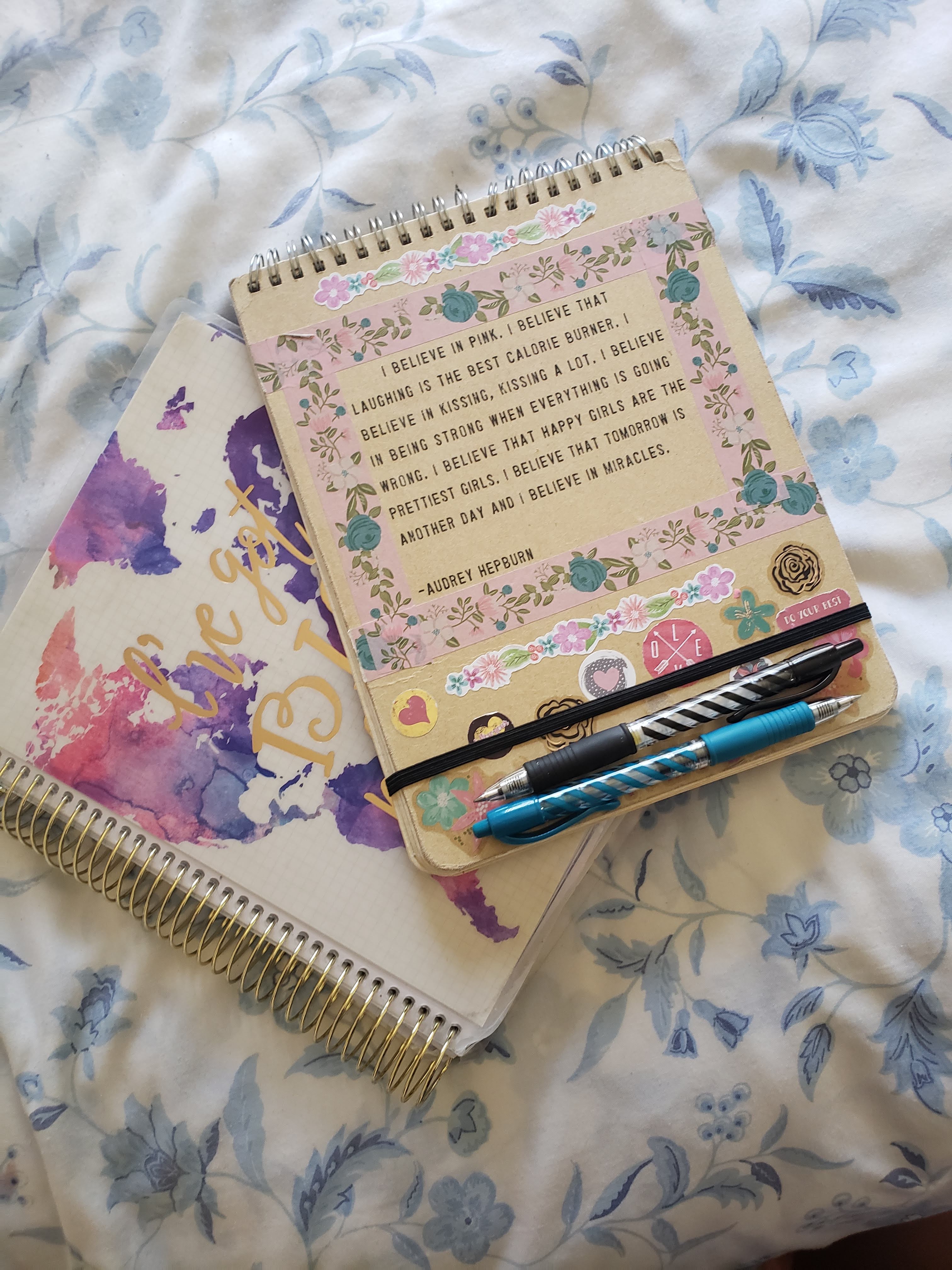 The one on top with the pens is my journal. The one underneath it is my planner. On the cover of my journal is a quote from Audrey Hepburn, who is iconic.
