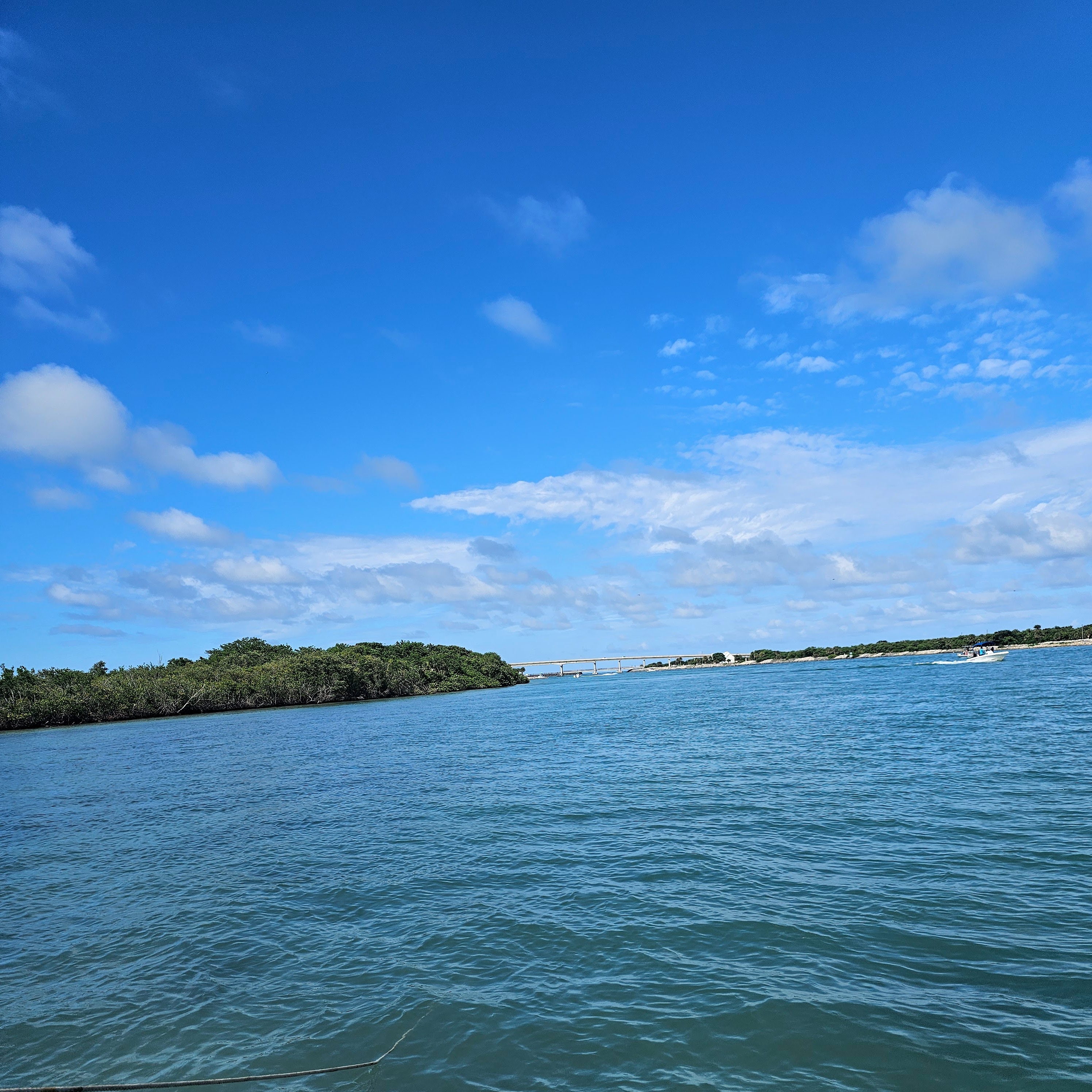 A photo of the blue sky with a bridge in the distance with some land and water at the fore front.