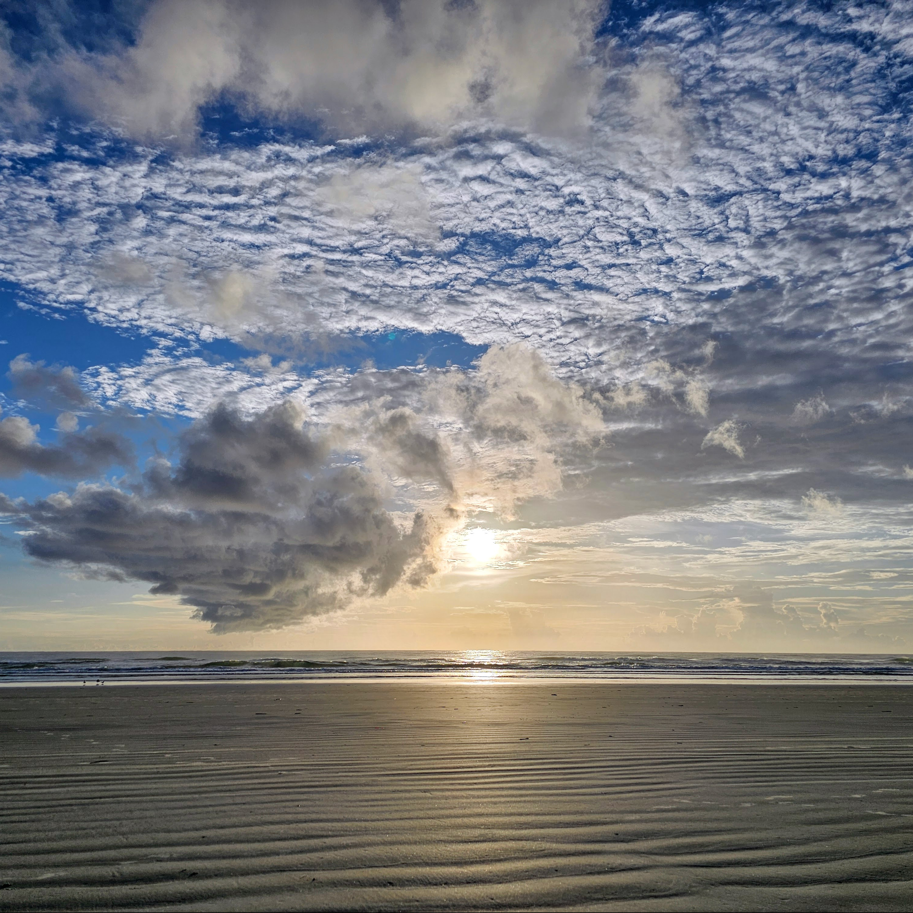 A sun rising above the ocean and into the clouds on the beach.